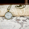 Brass pendant necklace holding quote from book about wizard Harry Potter with gold chain on a lace backdrop