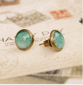 Two vintage studs brass with floral print under glass sitting on card with writing on it