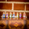 Seven vials filled with various colored fairy dust each with their own label like poison, sleeping beauty, kiss the girl and each with their own charm on top of book binding in front of brick wall