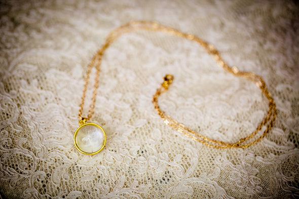 Gold plate dandelion seed necklace with a single seed lying on lace