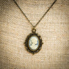 Cameo Necklace dusty muted blue and white on brass filigree charm pendant with brass chain on burlap linen backdrop