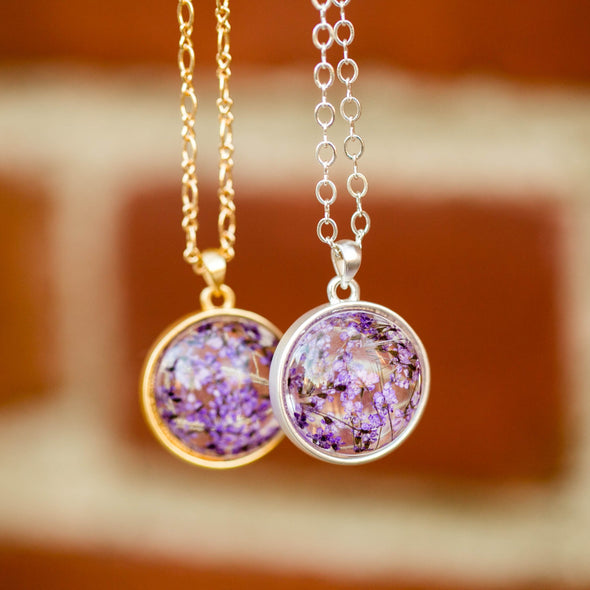 purple dried flower orb silver necklace hanging with brick wall background