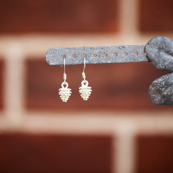 tiny gold pine corn earrings hanging on a purple flower, zoomed out