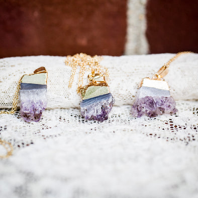 three raw amethyst necklace on gold chains displayed on lace with brick background