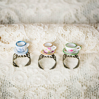 Three floral pattern vintage dollhouse tea cup and saucer rings with brass bands on lace backdrop