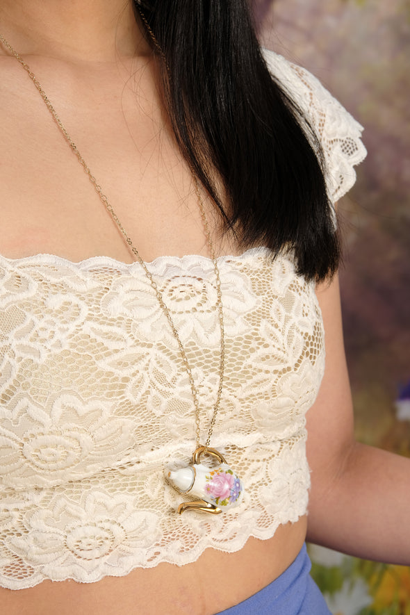 Beautiful model wearing floral teapot necklace on chainwearing lace crop top against tree backdrop