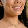 Beautiful model wearing gold ayame blossom stud earrings and gold chain orchid blossom necklace smiling in front of tree and flower backdrop