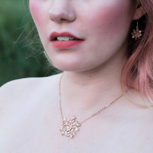 Beautiful model with pink hair wearing gold tree necklace and flower earrings lotus or water lily