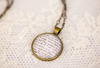 custom pendant necklace containing handwritten quote on lined paper with brass chain on lace 