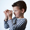 Cute child in striped shirt looks through working spyglass necklace on white background