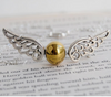 Golden ball with silver wing snitch like necklace sitting atop a page from a Harry potter book depicting a Quidditch match