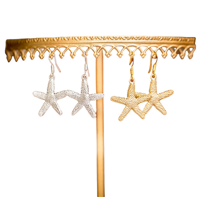 silver and gold starfish or seastar charm dangle earrings on gold earring display on white background 