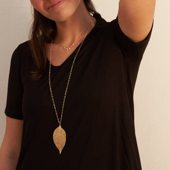 smiling israeli model wearing a laser cut gold leaf long necklace and matching earrings side angle