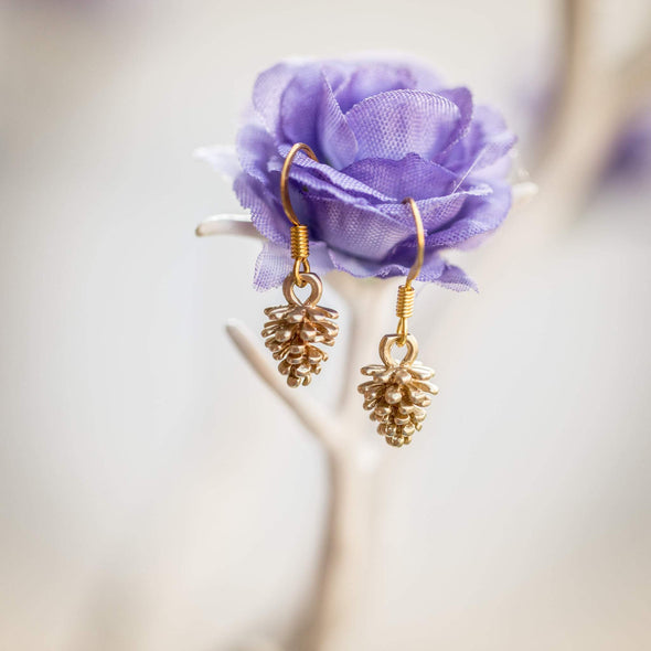 tiny gold pine corn earrings hanging on a purple flower
